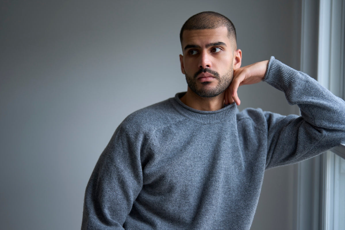 Man wearing a gray sweater against a plain wall